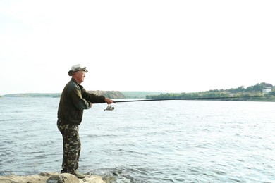 Fisherman with rod fishing near lake at summer