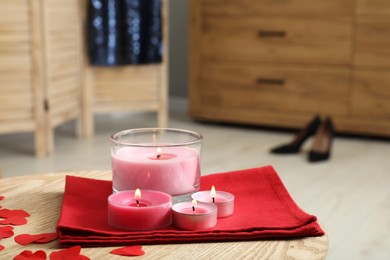 Photo of Burning candles, napkin and decorative hearts on wooden table indoors, closeup. Space for text