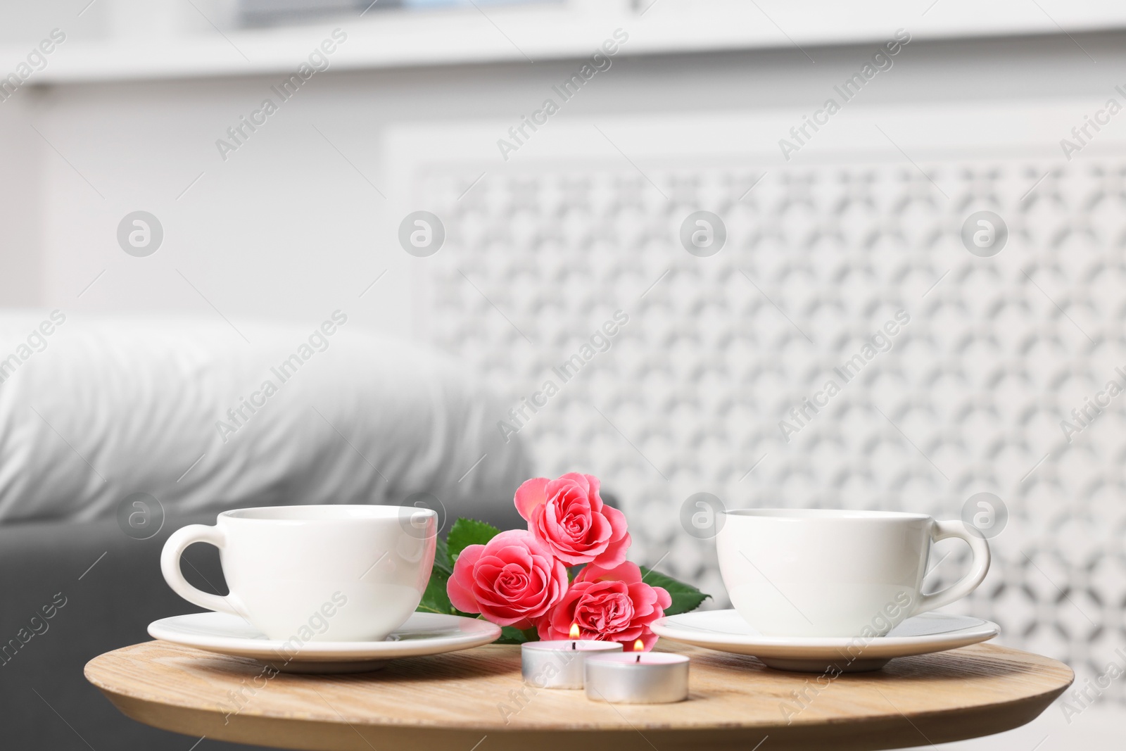 Photo of Burning candles, two cups of drink and flowers on coffee table indoors. Space for text