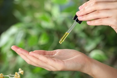 Photo of Woman dripping tincture from pipette onto hand against blurred green background, closeup