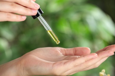 Photo of Woman dripping tincture from pipette onto hand against blurred green background, closeup