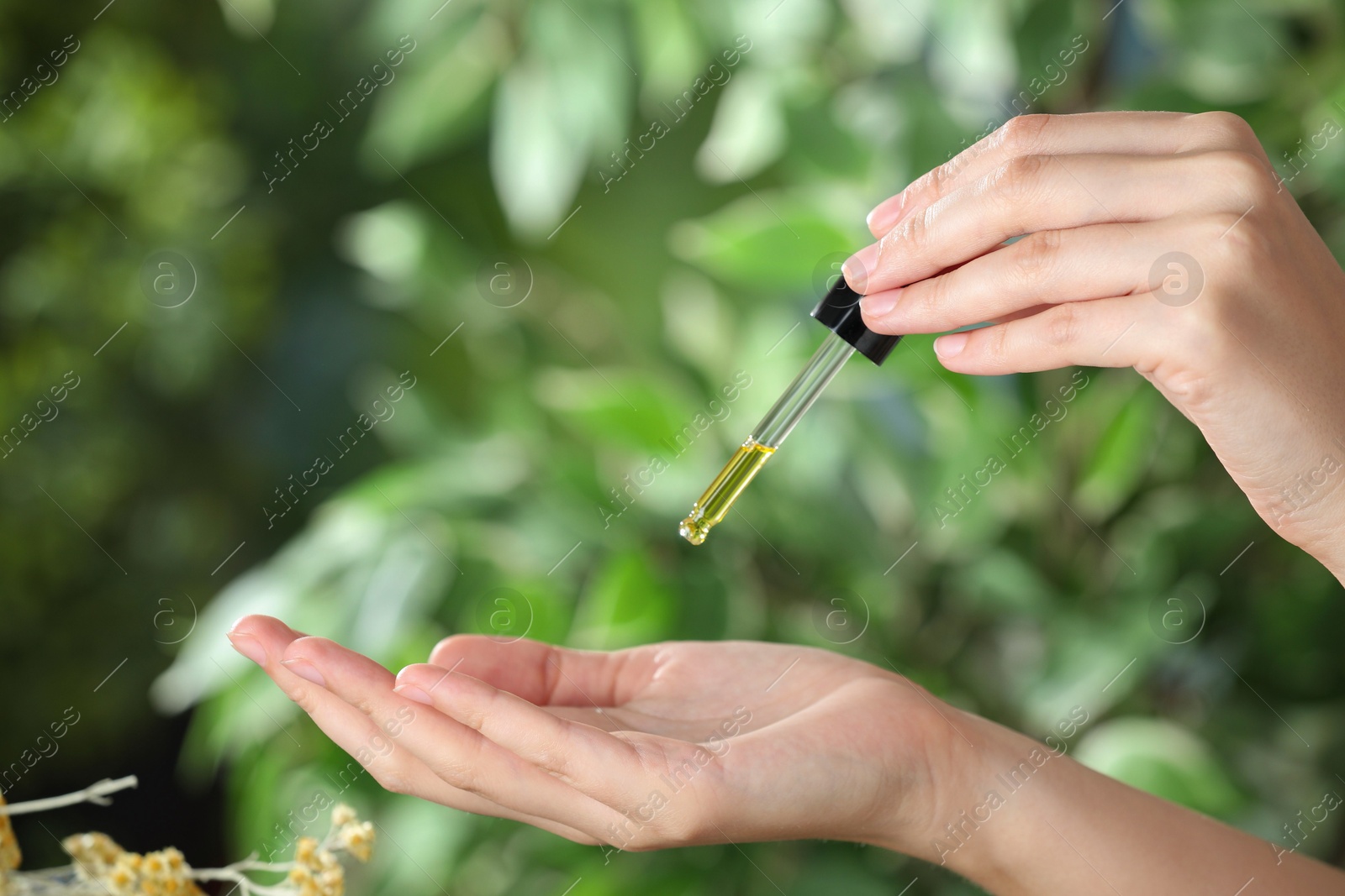 Photo of Woman dripping tincture from pipette onto hand against blurred green background, closeup