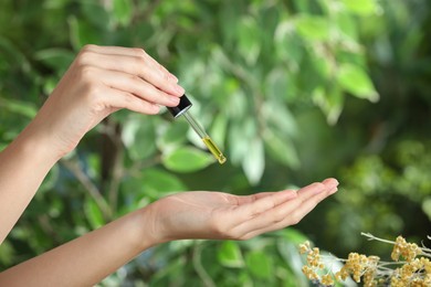 Woman dripping tincture from pipette onto hand against blurred green background, closeup