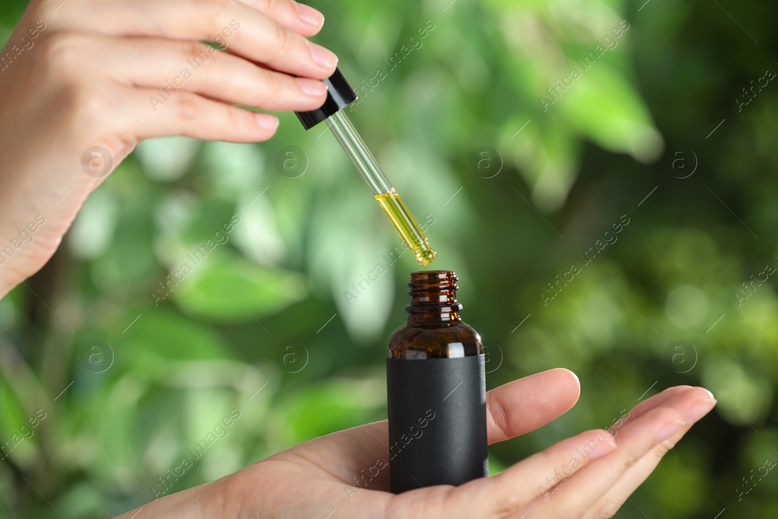 Photo of Woman dripping tincture from pipette into bottle against blurred green background, closeup