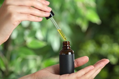 Photo of Woman dripping tincture from pipette into bottle against blurred green background, closeup