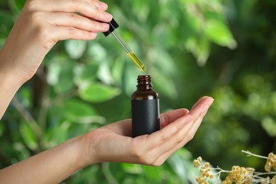 Photo of Woman dripping tincture from pipette into bottle against blurred green background, closeup