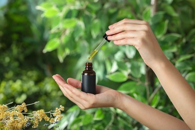 Photo of Woman dripping tincture from pipette into bottle against blurred green background, closeup