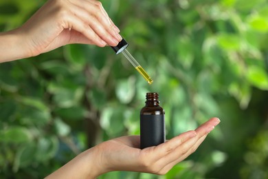 Photo of Woman dripping tincture from pipette into bottle against blurred green background, closeup