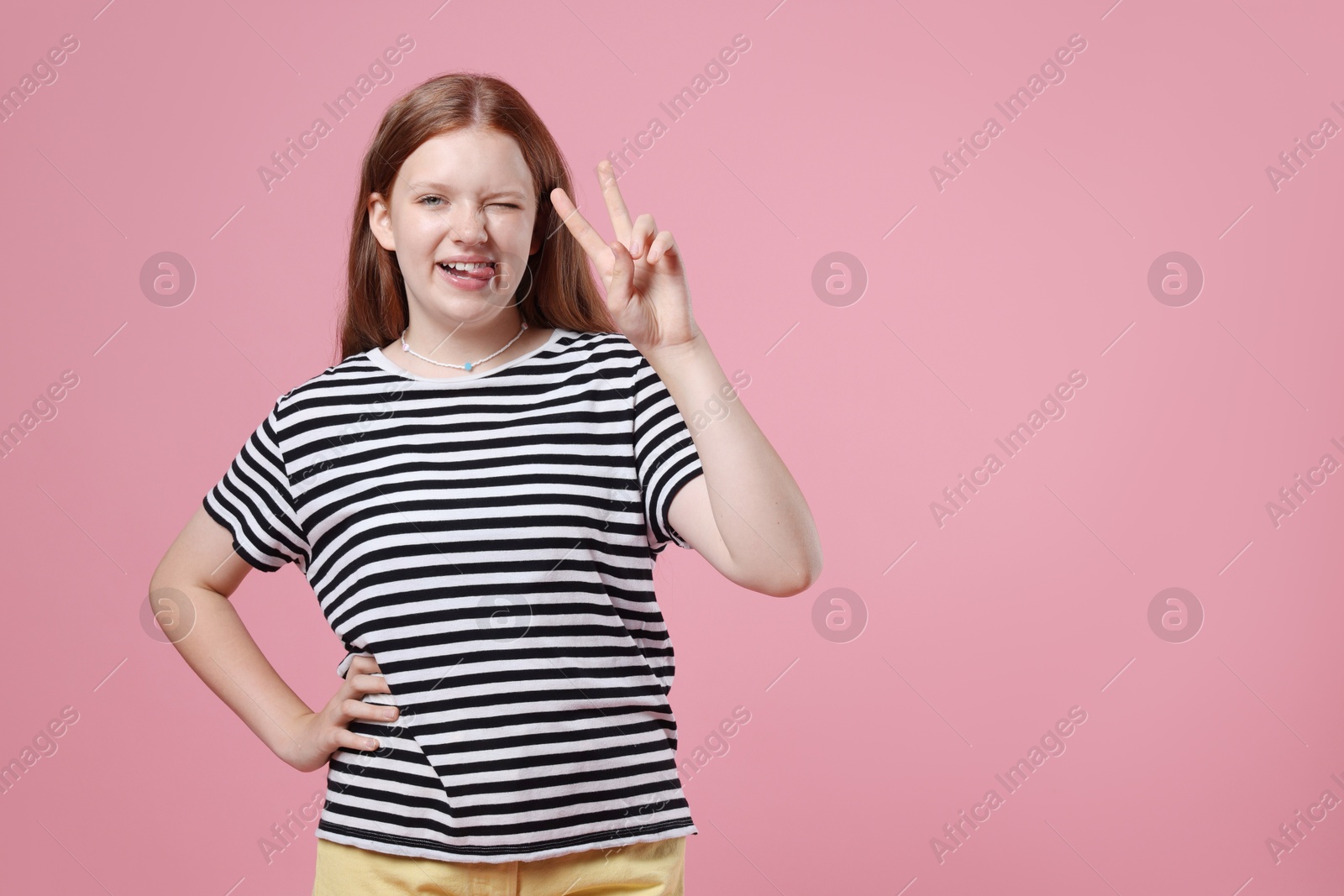 Photo of Teenage girl with showing tongue and v-sign on pink background, space for text