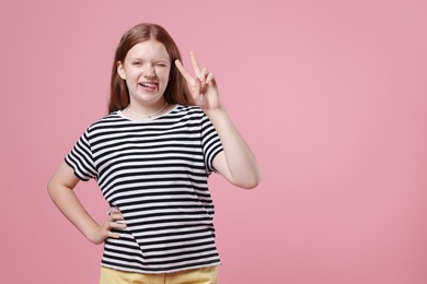 Teenage girl with showing tongue and v-sign on pink background, space for text