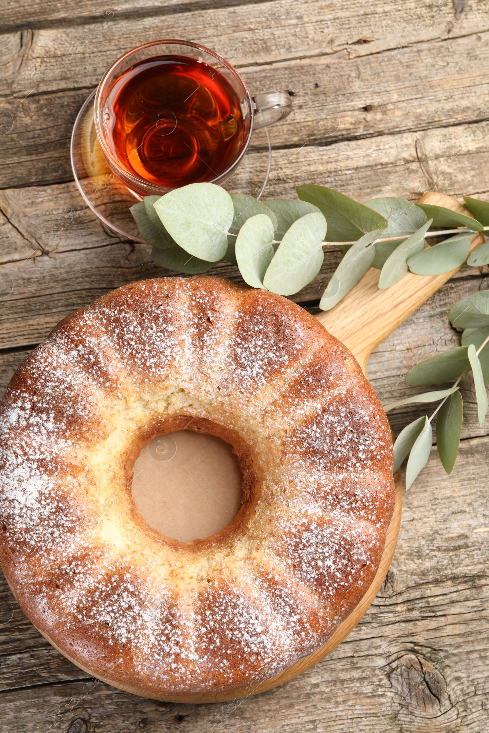 Photo of Freshly baked sponge cake, tea and eucalyptus leaves on wooden table, top view