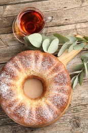 Freshly baked sponge cake, tea and eucalyptus leaves on wooden table, top view