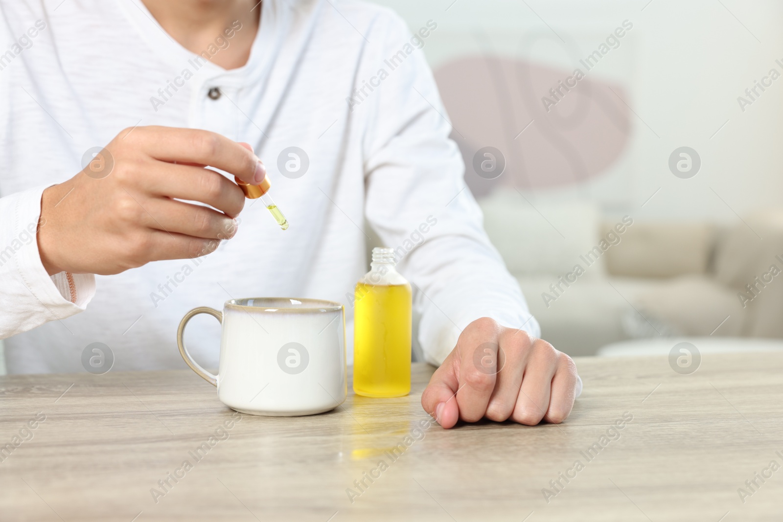 Photo of Young man dripping CBD tincture into drink at wooden table, closeup