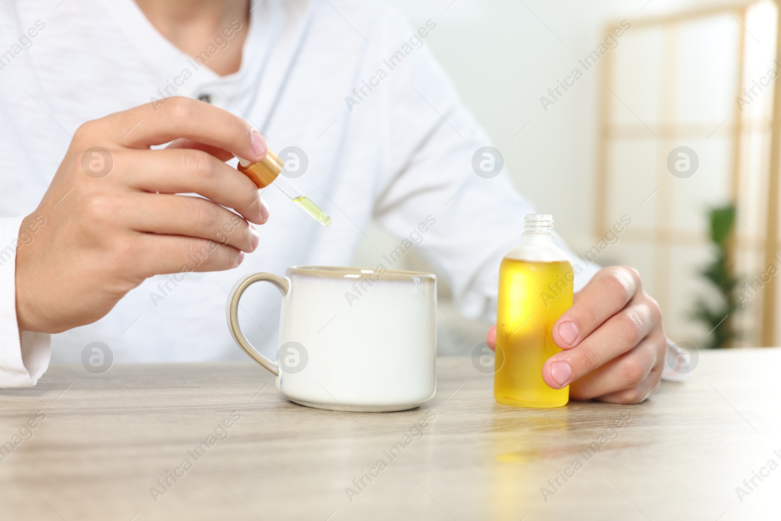 Photo of Young man dripping CBD tincture into drink at wooden table, closeup