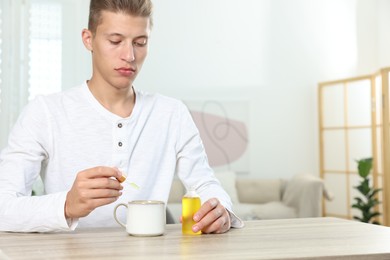 Photo of Young man dripping CBD tincture into drink at wooden table, space for text