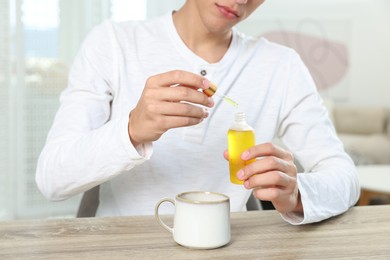 Photo of Young man dripping CBD tincture into drink at wooden table, closeup