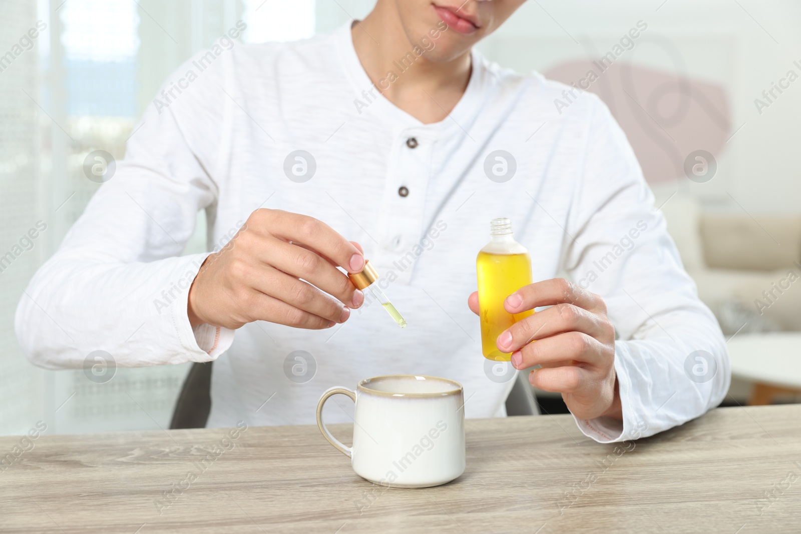 Photo of Young man dripping CBD tincture into drink at wooden table, closeup