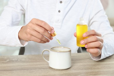 Photo of Young man dripping CBD tincture into drink at wooden table, closeup