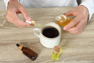 Photo of Young man dripping CBD tincture into drink at wooden table, closeup