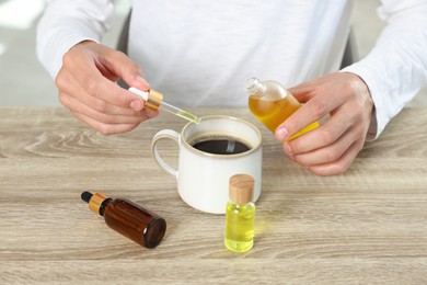 Young man dripping CBD tincture into drink at wooden table, closeup