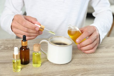 Photo of Young man dripping CBD tincture into drink at wooden table, closeup