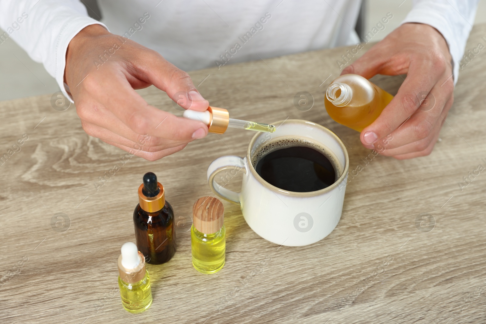 Photo of Young man dripping CBD tincture into drink at wooden table, closeup