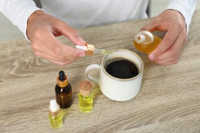 Young man dripping CBD tincture into drink at wooden table, closeup