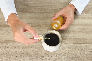 Photo of Young man dripping CBD tincture into drink at wooden table, above view