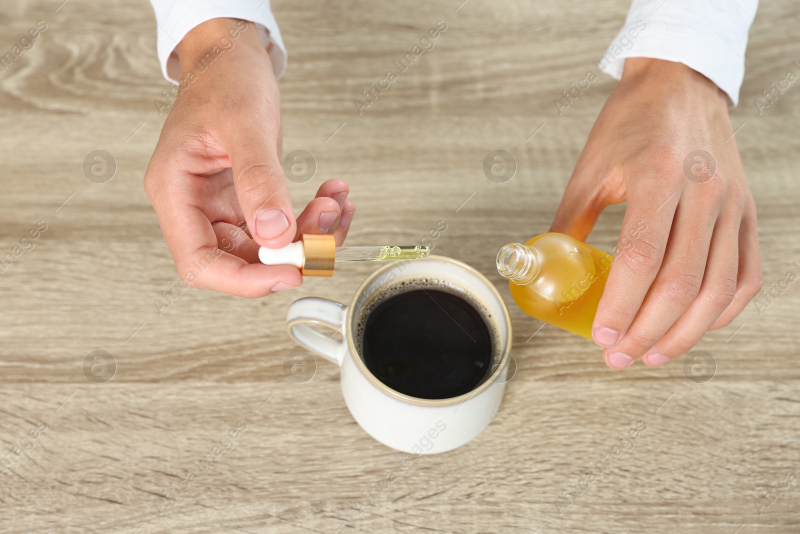 Photo of Young man dripping CBD tincture into drink at wooden table, above view