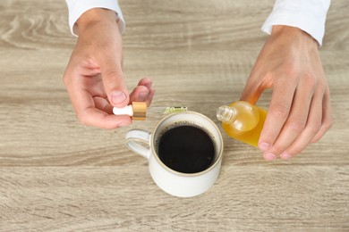 Photo of Young man dripping CBD tincture into drink at wooden table, above view