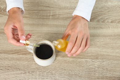 Photo of Young man dripping CBD tincture into drink at wooden table, above view