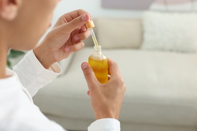 Photo of Young man taking CBD tincture indoors, closeup