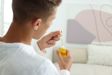 Photo of Young man taking CBD tincture indoors, closeup. Space for text