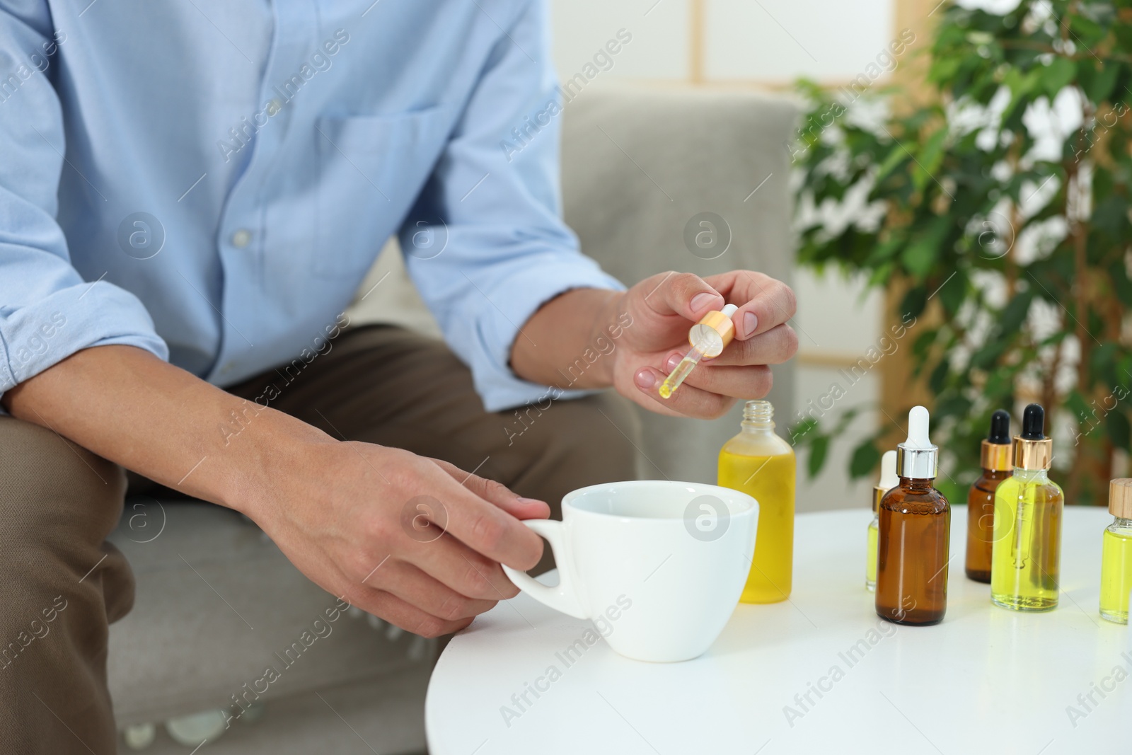 Photo of Young man dripping CBD tincture into drink at white table, closeup