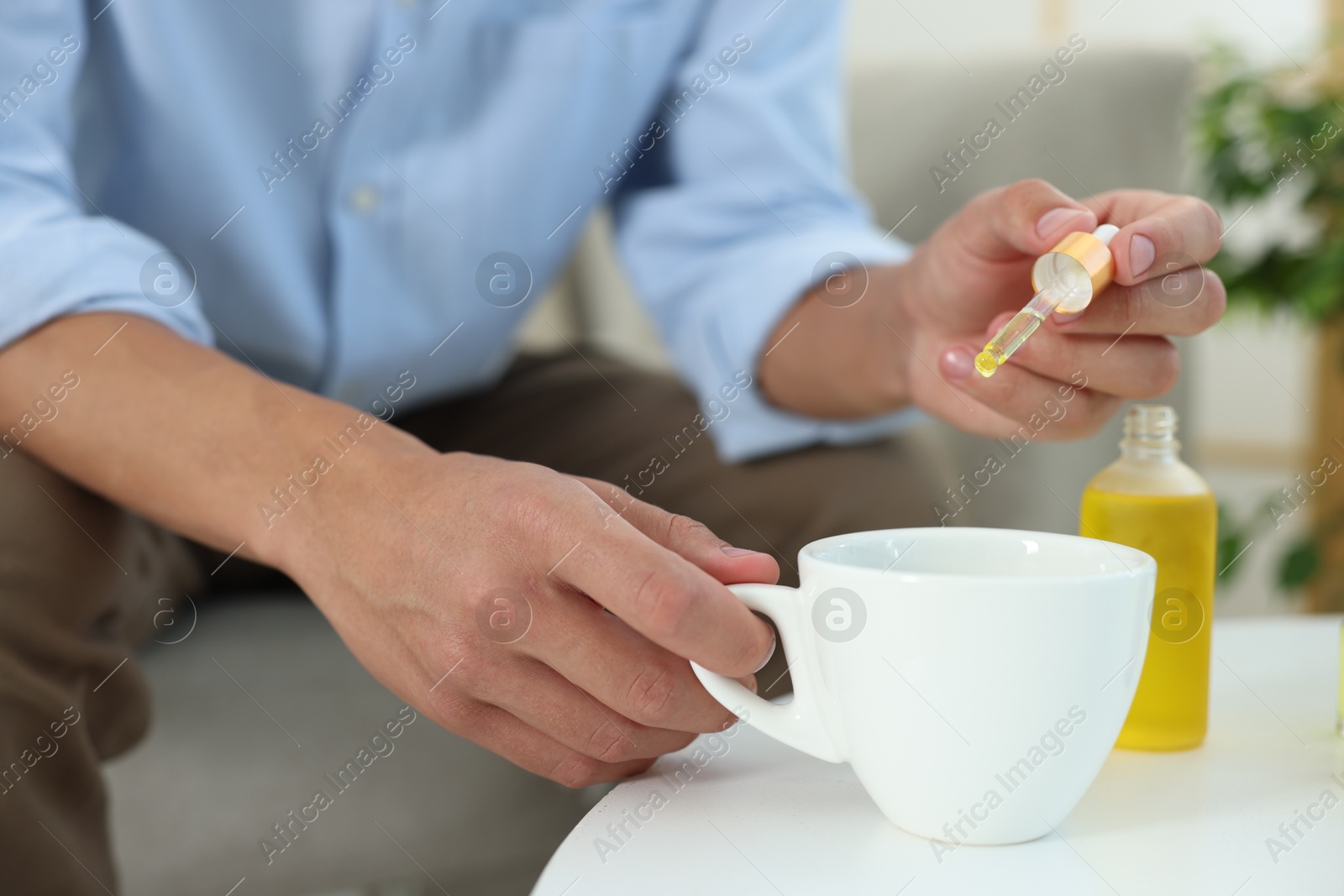 Photo of Young man dripping CBD tincture into drink at white table, closeup