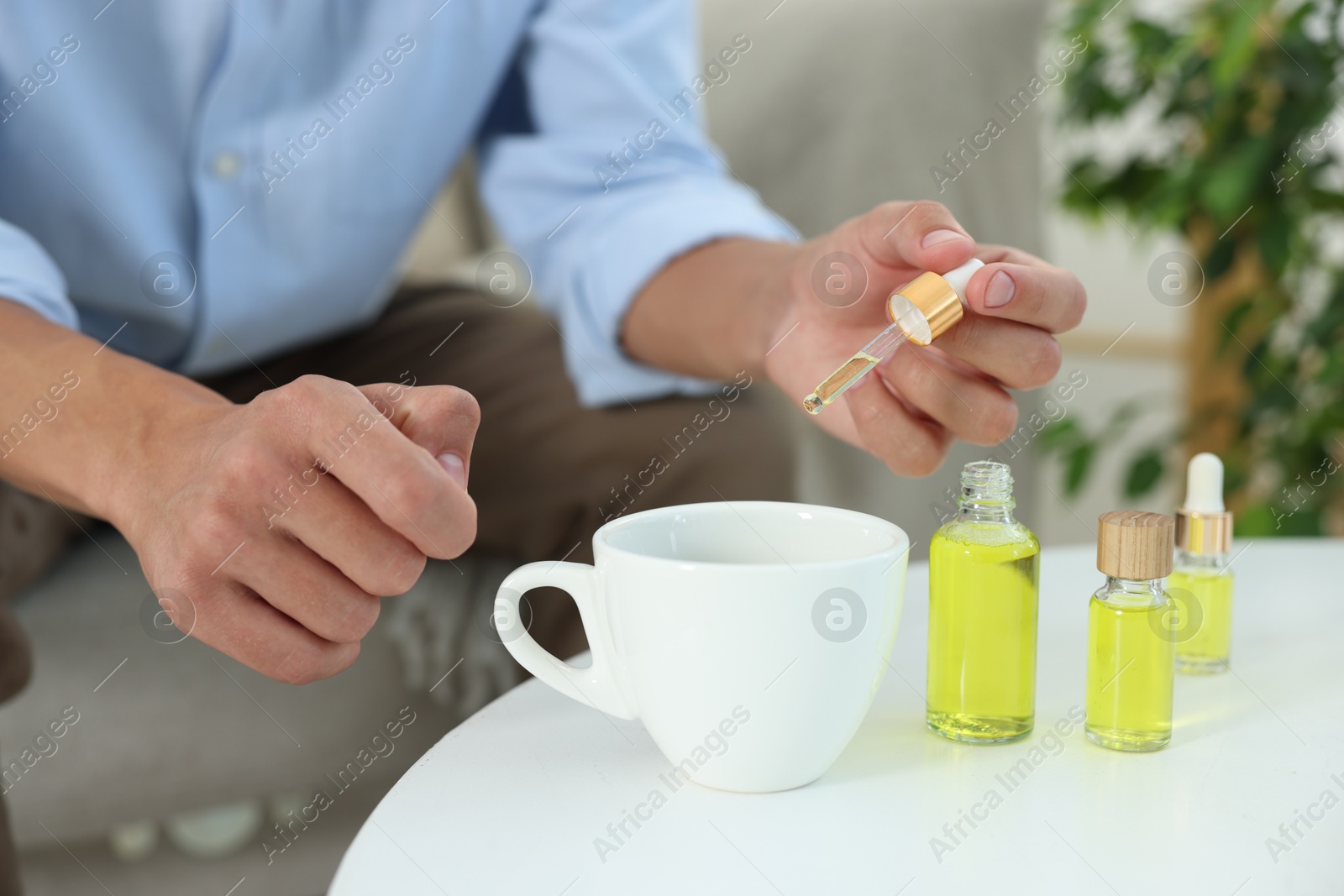 Photo of Young man dripping CBD tincture into drink at white table, closeup