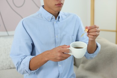 Photo of Young man dripping CBD tincture into drink indoors, closeup