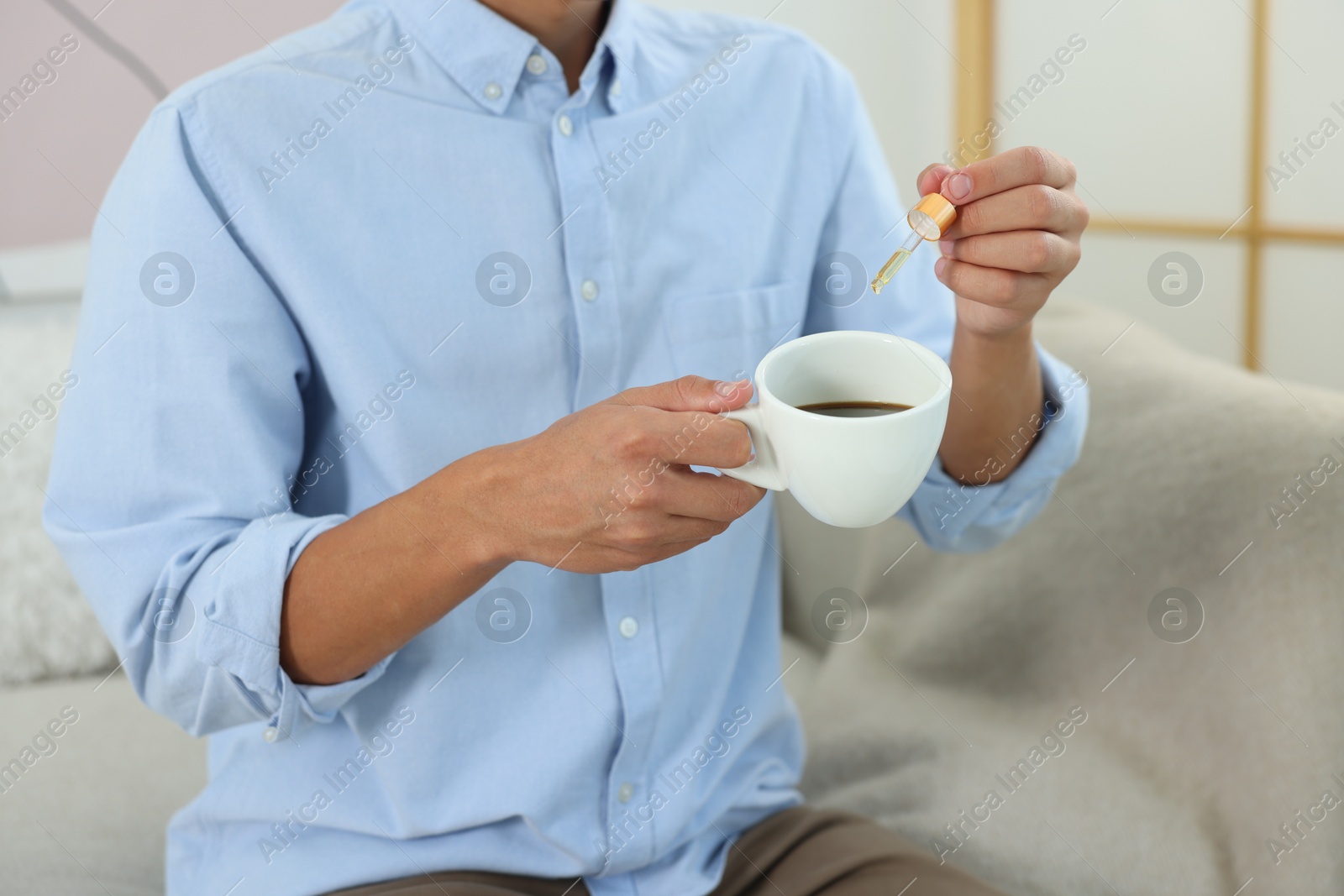 Photo of Young man dripping CBD tincture into drink indoors, closeup