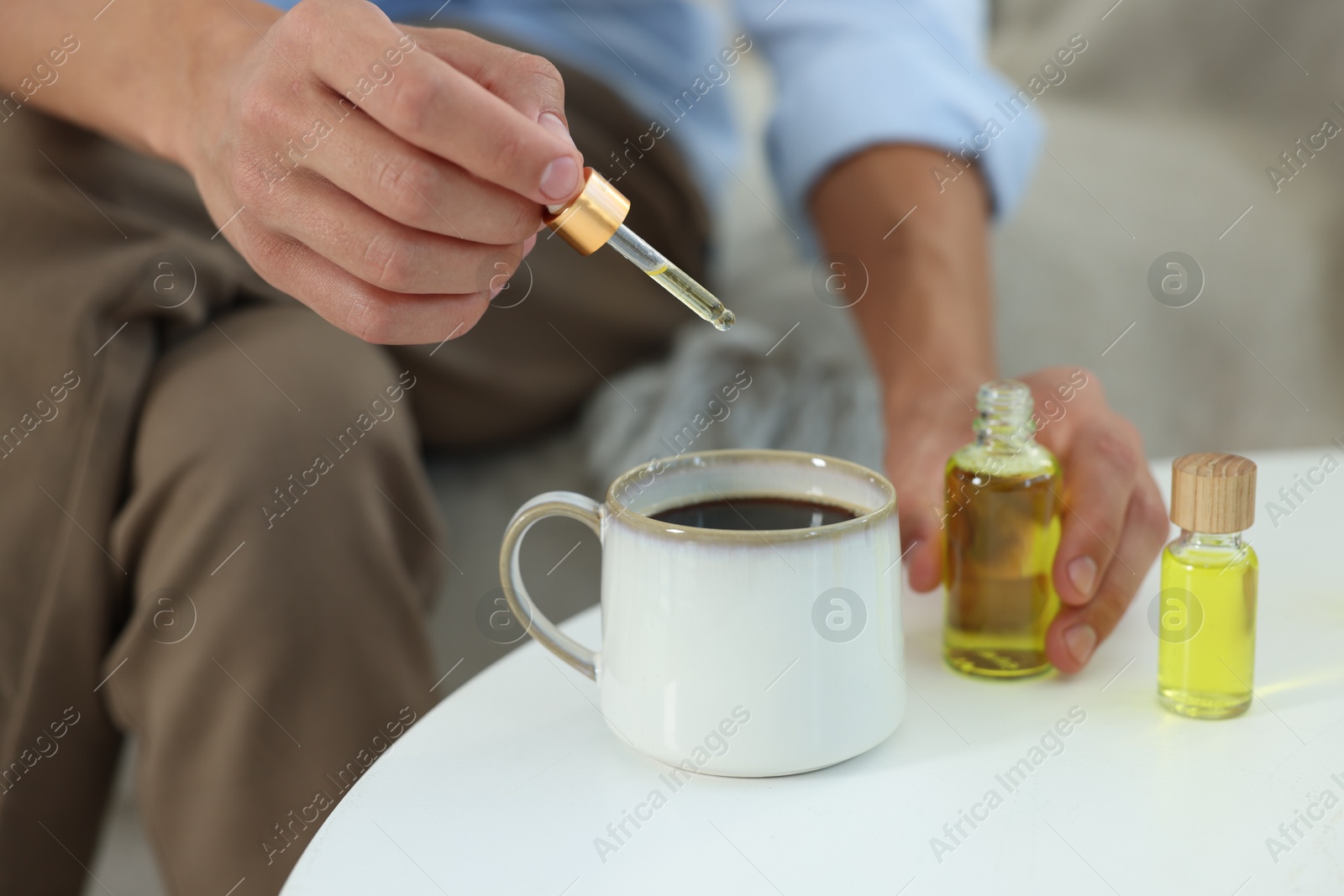 Photo of Young man dripping CBD tincture into drink at white table, closeup