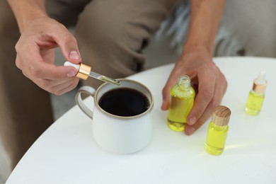 Photo of Young man dripping CBD tincture into drink at white table, closeup