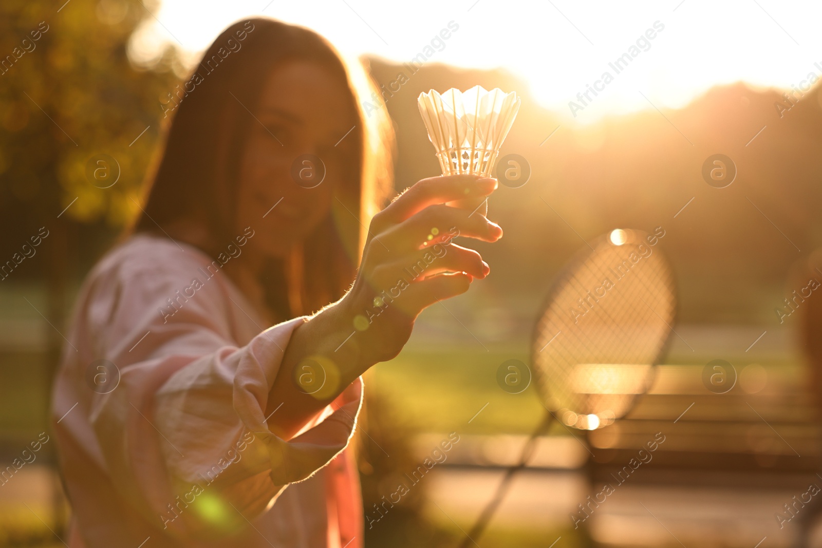 Photo of Happy young woman with badminton racket and shuttlecock in park on sunny day, selective focus