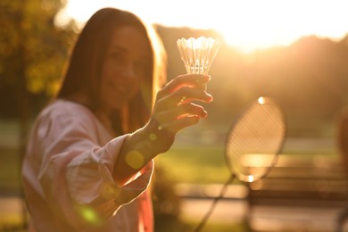 Happy young woman with badminton racket and shuttlecock in park on sunny day, selective focus