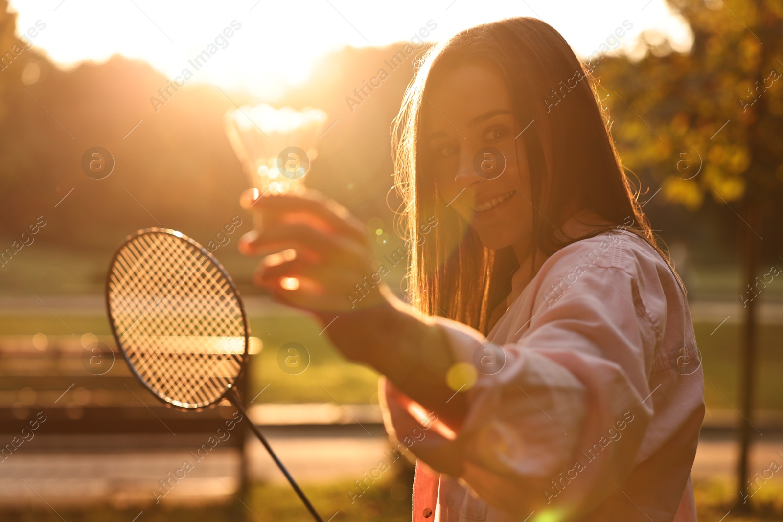 Photo of Happy young woman with badminton racket and shuttlecock in park on sunny day, selective focus