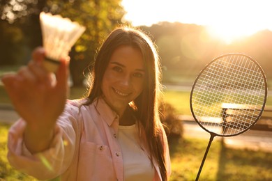 Happy young woman with badminton racket and shuttlecock in park on sunny day, selective focus