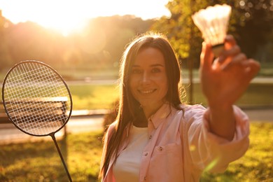 Photo of Happy young woman with badminton racket and shuttlecock in park on sunny day, selective focus