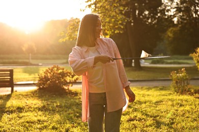 Happy young woman with badminton racket and shuttlecock in park on sunny day