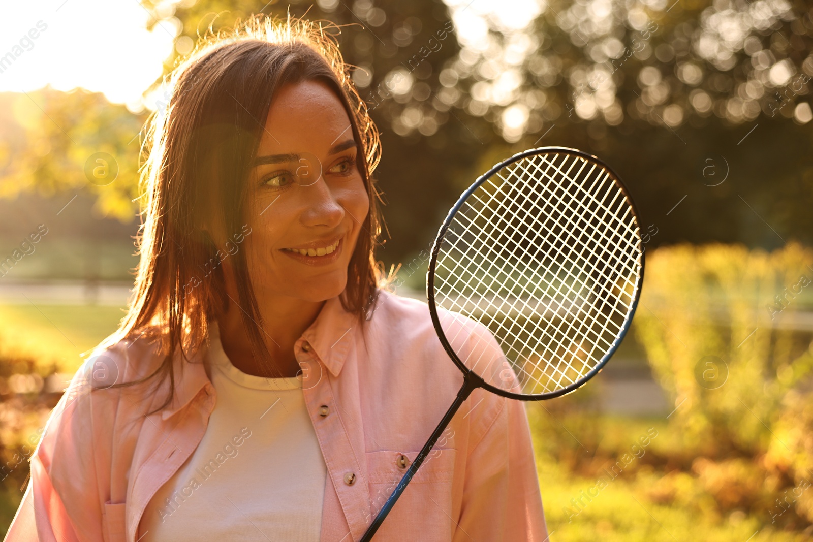 Photo of Happy young woman with badminton racket in park on sunny day