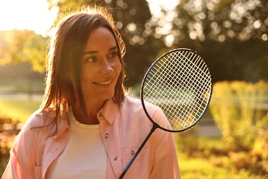 Happy young woman with badminton racket in park on sunny day