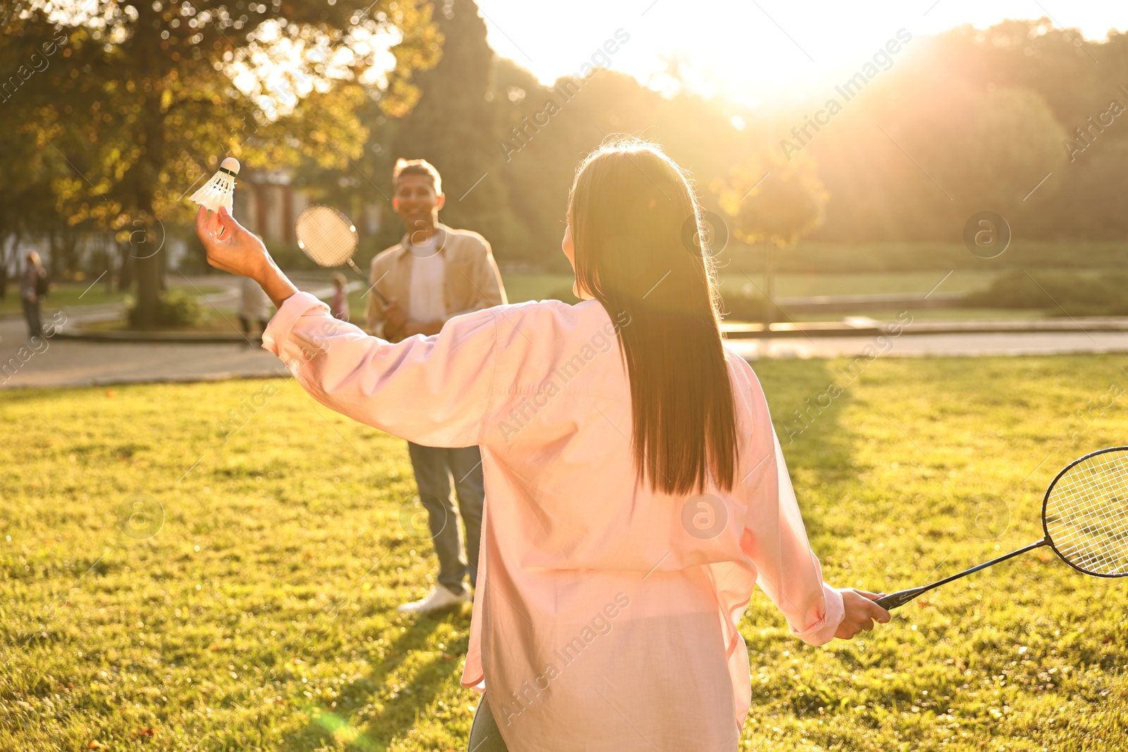 Photo of Young woman and man playing badminton in park on sunny day, selective focus