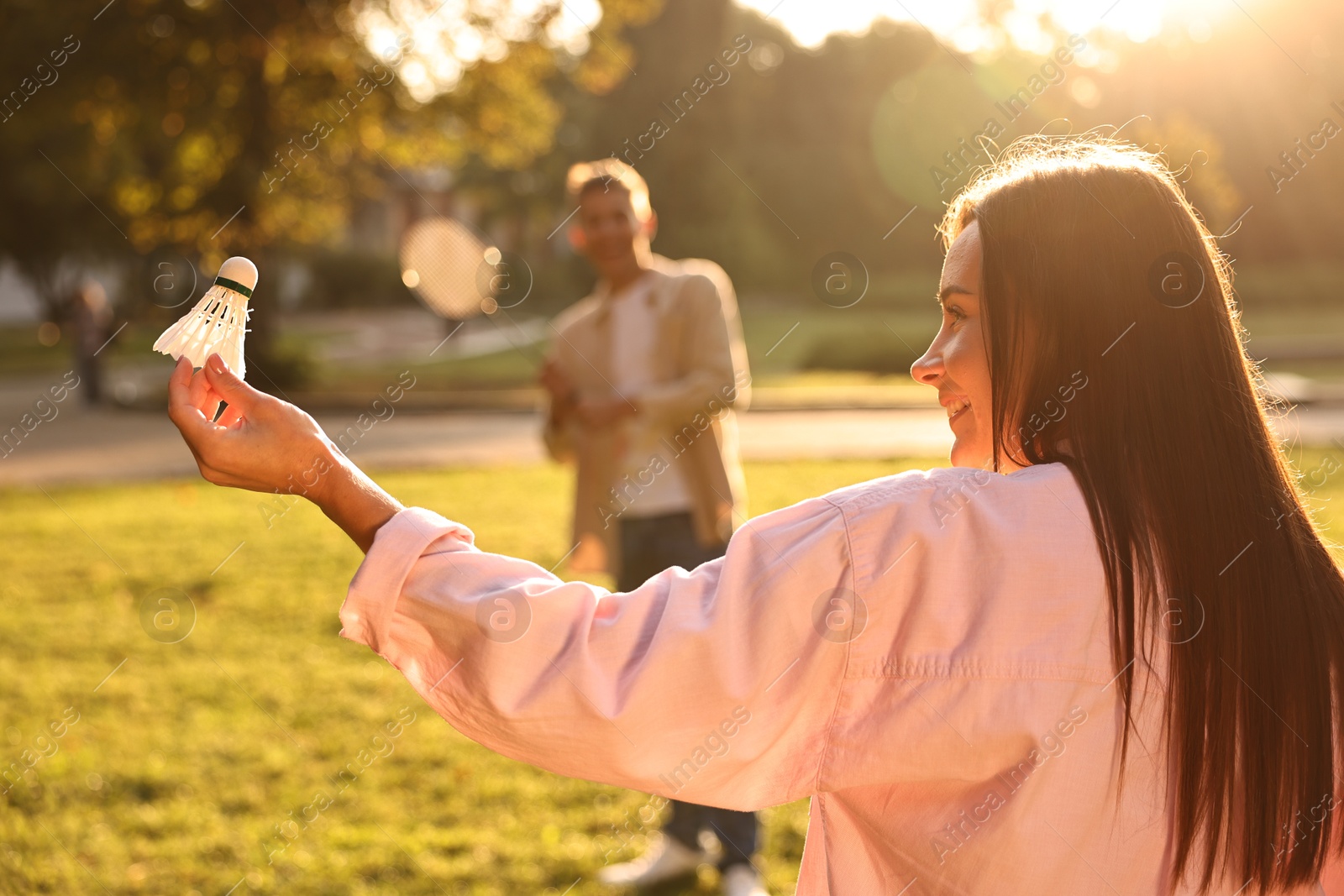 Photo of Young woman and man playing badminton in park on sunny day, selective focus